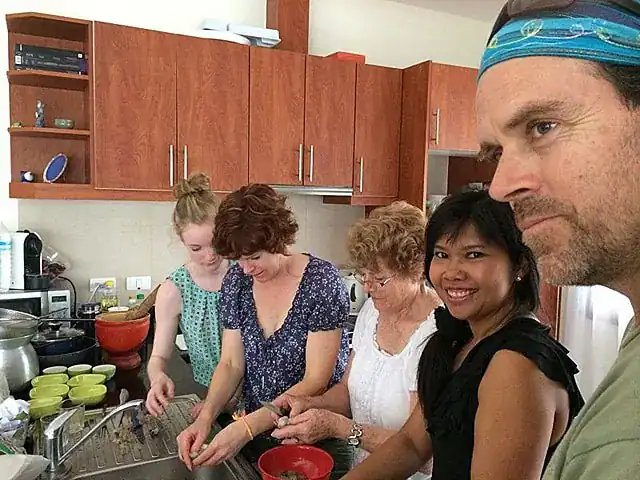 Supparin teaching a private Thai cooking class in Phuket with guests around a kitchen island